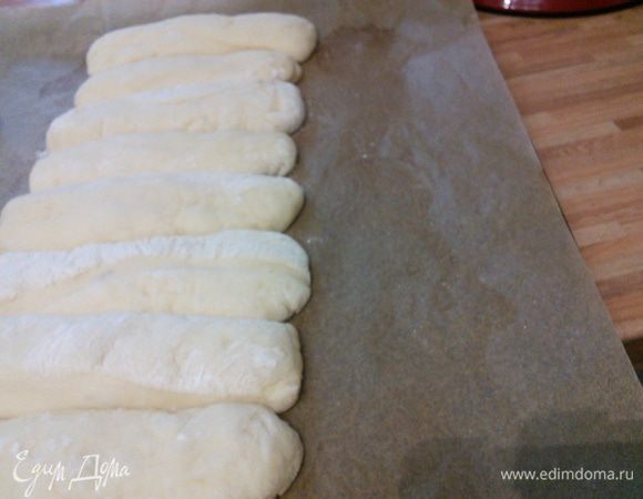 Тесто делим на 7 частей, даём отдохнуть 10 минут. Придаём нашим заготовкам форму продолговатых пирожков и слегка их приплюскиваем с помощью ладошки. Укладываем на пергамент длинной стороной рядом друг с другом. 