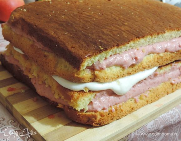 Далее накрываем вторым пластом бисквита срезом вниз. Смазываем примерно третью сливочного крема, далее снова бисквит и оставшийся клубничный крем.