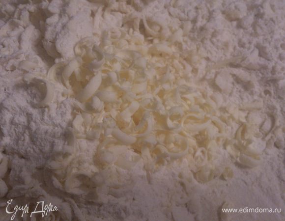 Муку просеять горкой на рабочий стол. Сверху быстро натереть сливочное масло на крупную терку.