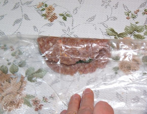 Движением вниз и на себя продолжайте тянуть целлофан, заворачивая начинку в котлету. Получится рулет. 