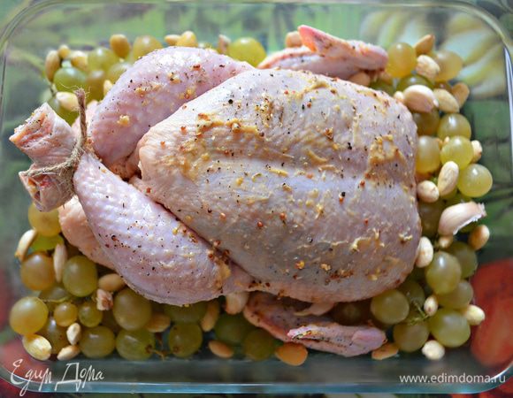 Вокруг курицы выложите гроздочки винограда, зубчики чеснока и очищенный миндаль. Несколько ягод винограда и зубчик чеснока положите внутрь курицы. Влейте в форму вино. Запекайте курочку при 230°C в течение 15 мин, затем убавьте нагрев до 180°C-190°C и готовьте ещё 1 час. 