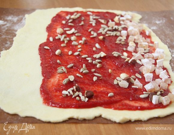 Рулетиков будет 4, поэтому делим клубничный джем, орехи и лукум тоже на 4. Смазать тесто 100 граммами клубничного джема, на одном конце оставить тесто без начинки примерно 2-3 см, присыпать начинку орехами-семечками. По длинному краю выложить полоску из лукума. Завернуть рулет, начиная с "лукумной" стороны.