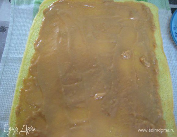 Готовый бисквит положить на чистое полотенце бумагой вверх, аккуратно ее снять. Намазать горячий бисквит сгущенкой.