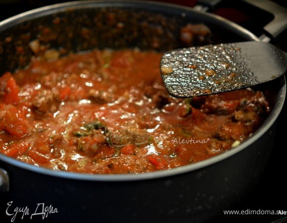 Добавить томаты баночные порезанные кубиками, изюм белый, вино, томатную пасту, сахар, базилик, соль и черный перец. Довести до кипения. Убавить огонь и тушить без крышки 15 минут.