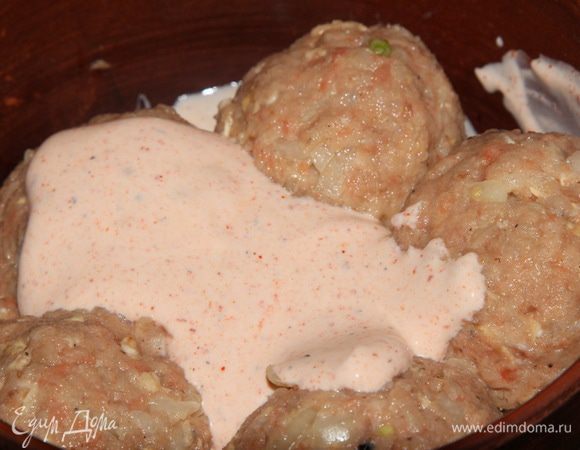 Берем емкость для запекания, у меня керамическая миска, на дно миски выкладываем пару ложек сметаны, затем в один слой фрикадельки и поливаем соусом.