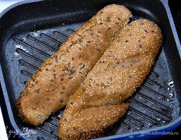 Багет разрезать вдоль пополам, не прорезая с одной стороны до конца, сбрызнуть внутри оливковым маслом, выложить разрезом вниз на сковороду-гриль и обжаривать до появления золотистых полосок.