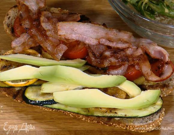 Обжаренный багет смазать внутри оставшейся заправкой, выложить на одну сторону цукини, кружки лимона и авокадо, на другую — помидоры и сало.