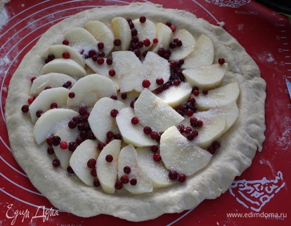 Поднявшееся тесто разделить на две неравные половинки, большую половинку раскатать и уложить в форму на 28, сделав бортики. Яблоки порезать дольками, выложить на тесто, посыпать ягодой и сахаром.