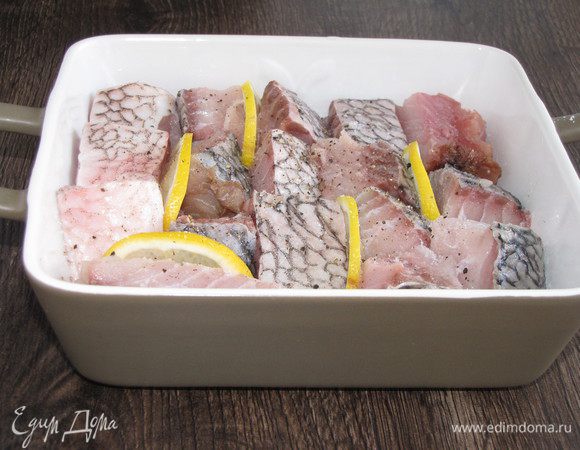 На лук выложить кусочки рыбы. Между ними проложить кружки лимона.
