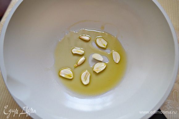В сковороду влить оливковое масло, нагреть на среднем огне. Добавить порезанный на ломтики чеснок.