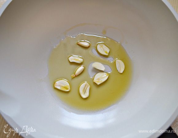 В сковороду влить оливковое масло, нагреть на среднем огне. Добавить порезанный на ломтики чеснок.