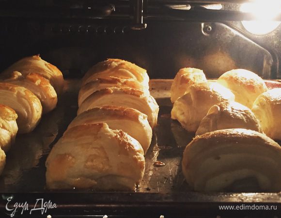 Получившиеся слойки нужно выложить на смазанный или застеленный пергаментом противень. Одно оставшееся яйцо взбить вилочкой в стакане и кистью смазать слойки. Выпекать на 180°C примерно 20-25 минут.