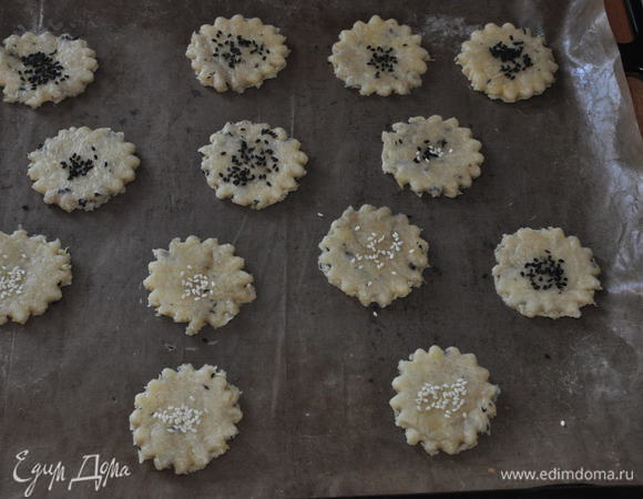 Тесто раскатать толщиной 3-4 мм (печенье еще немного подрастет в духовке) и фигурной выемкой вырезать печенье. 
Переложить на противень, застеленный пергаментом (у меня тефлоновый лист), слегка смазать середину взбитым белком и присыпать сушеным базиликом или тимьяном. Я присыпала черным и белым кунжутом.
