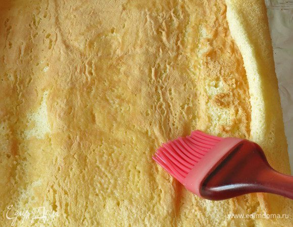 Рулет остыл, аккуратно разворачиваем. Переносим его на фольгу. Получаются два края со сгибом. Готовим пропитку — в теплой воде растворяем 1 чайную ложку сахара, можно добавить коньяк. Пропитываем корж.
Намазываем крем.
