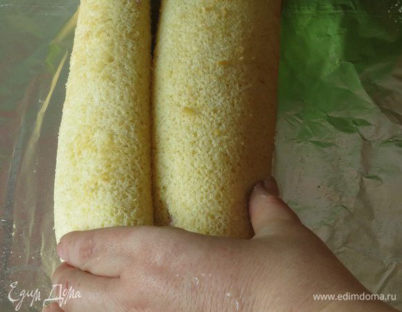 Сворачиваем слева и справа бисквит. Закрепляем все фольгой — заворачиваем, можно использовать и пленку. Замечаем, где соединение роллов.