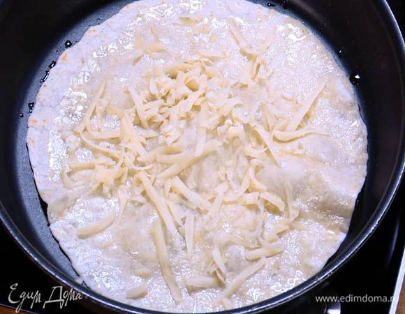 Разогреть в отдельной сковороде оставшееся оливковое масло и прогреть тортилью, затем перевернуть и посыпать натертым сыром. Когда сыр слегка расплавится, перевернуть лепешку еще раз, снова посыпать сыром и переложить на тарелку. Так же прогреть вторую тортилью.