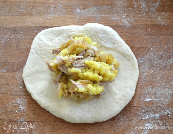 Подошедшее тесто выложить на припыленную мукой рабочую поверхность и слегка обмять. Разделить на 12 равных кусочков, весом около 95 см каждый. Из каждого кусочка сформировать лепешку. Выложить в центр начинку.