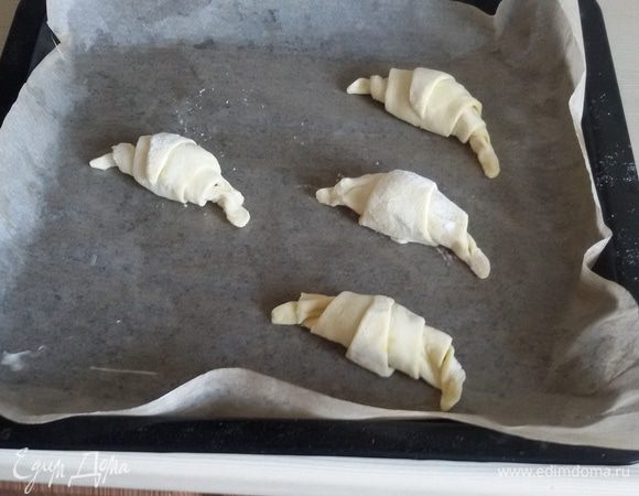 Предварительно разогреть духовку до 200°С.
Выстелить противень бумагой для выпечки и смазать сливочным маслом.
Выложить на бумагу круассаны и поставить в духовку. Выпекать при температуре 190°С 10-15 минут до зарумянивания корочки.
