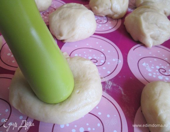 Наше тесто готово. Выкладываем его на стол, припыленный мукой, обминаем и делим на 10-12 частей. Из каждой части делаем шарик, укладываем сразу на противень, застеленный пекарской бумагой или силиконовым ковриком. Теперь делаем удобным предметом углубление (у меня это ручка скалки), если необходимо, можно увеличить углубление руками).