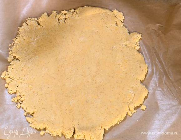 Поместить тесто между двумя слоями бумаги для выпечки и раскатать скалкой в корж, затем верхний слой бумаги снять и уложить тесто вместе с нижним слоем бумаги в разъемную форму, сформировав бортики.