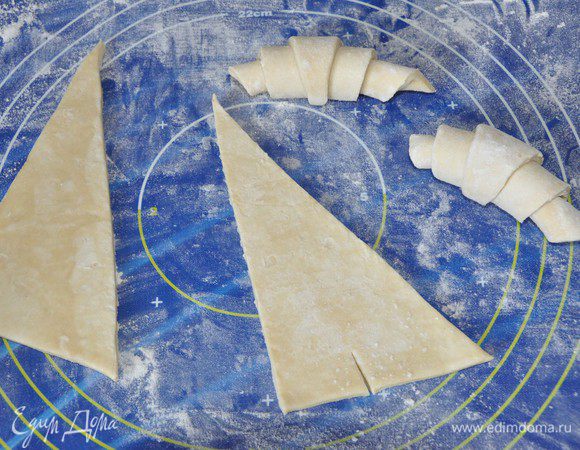 Это тесто не нуждается в раскатывании.
Тесто разделить на 2 равных прямоугольника, каждый разрезать на 2 треугольника. 
Треугольник надсечь у основания, скрутить тесто от широкого края к узкому, спрятать узкий край под круассан. Придать форму полумесяца, выложить на противень, застеленный бумагой для выпечки. Накрыть салфеткой и дать подойти тесту в течение 1,5 часов.
