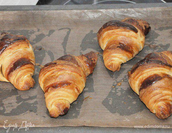 Духовку включить разогреваться до 210°C. 
Смазать круассаны взбитым яйцом, стараясь не попадать на срезы, чтобы слои не склеивались. Выпекать в разогретой духовке при 180-200°C 15-20 минут до золотистого цвета. 
Полностью отсудить.
