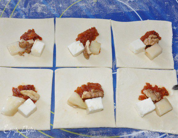 Тесто раскатать тонко, но следить, чтобы оно не порвалось.
Нарезаем на квадраты и выкладываем по кусочку груши и сыра, половину чайной ложки томатов, половинку грецкого ореха. Начинку выкладываем вдоль диагонали, чтобы удобнее потом было складывать уголок. 
Края теста смазываем взбитым желтком. 