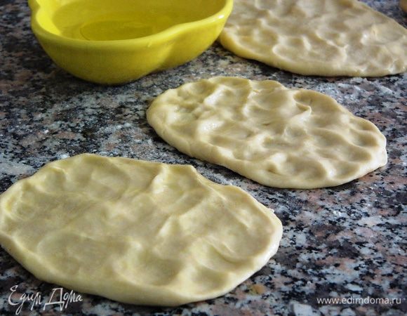 В небольшую мисочку наливаем воды и каплю оливкового масла. Смачивая руки водой, расплющиваем каждый шарик теста, придавая округлую форму лепешки. 