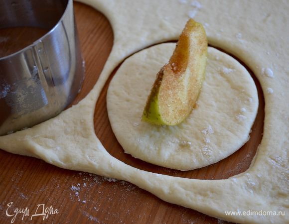 Выложить его на рабочую поверхность, слегка присыпанную мукой. Раскатать тесто в пласт толщиной около 7 мм и вырезать кружочки (у меня диаметром около 9 см). На каждый кружок теста положить дольку яблока.