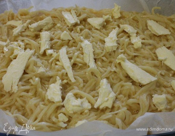 Форму для запекания выстелить пергаментом, смазать сливочным маслом и посыпать молотыми сухарями. Равномерно распределить лапшу и залить яичной смесью. Сверху распределить кусочки сливочного масла. Форму накрыть крышкой или фольгой. Запекать при 180°C 20 минут, затем крышку снять и запекать еще 20 минут, чтобы верх немного подрумянился.. Если у вас стеклянная форма для запекания, крышку можно не снимать.