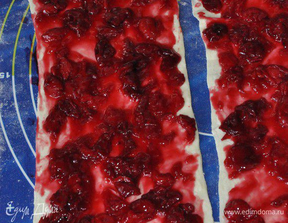 Слоёное тесто раскатать в одном направлении в прямоугольники размером 10-12 на 25-30 см. Нанести вишневую начинку, не доходя до короткого края теста пару сантиметров, чтобы потом можно было хорошо скрепить рулет.