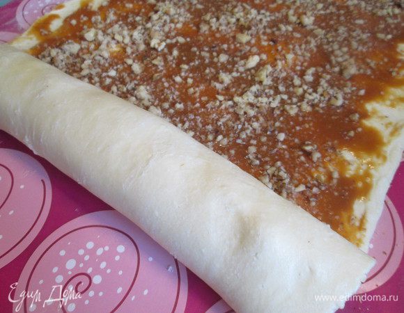 Смазываем пласт теста сгущенкой, посыпаем ореховой крошкой и скручиваем по длинной стороне, укладываем на шов.