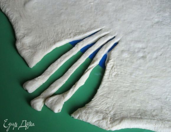 Посыпать поверхность немного мукой. Раскатать скалкой пласт овальной формы. С одного края сделать три глубоких разреза.