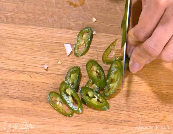 Перец чили вместе с семенами нарезать тонкими колечками, выложить к грибам с колбаской и беконом, все перемешать.