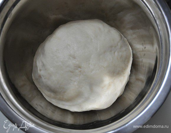 На хорошо присыпанную мукой поверхность выложить тесто и, постепенно добавляя оставшуюся муку, начать его вымешивать.
Муки может уйти чуть больше или меньше, в зависимости от качества муки, величины яиц и др. Муку добавлять, пока тесто не станет мягким, но слегка липнувшим к рукам. 
Вымешивать тесто в течение 10 минут, до тех пор пока оно не станет эластичным и не перестанет липнуть к рукам и поверхности. 
Выложить тесто в миску, слегка присыпать мукой, накрыть влажным полотенцем и убрать в теплое место без сквозняков. Я убираю в духовку, включенную в режим "Свет". Оставить тесто для подъема до увеличения в два раза.