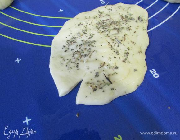 Каждый кусочек расплющить рукой в тонкую лепешку. Лепешка должна быть обмазана маслом с обеих сторон. Надрезать лепешку с широкого конца и обсыпать лепешку прованскими травами.