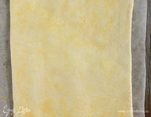 Тесто немного раскатайте на присыпанной мукой поверхности в прямоугольник толщиной 4 мм. Смешать яйцо с молоком. Смазать поверхность коржа яйцом, затем присыпать сахаром. Противень выстелить бумагой для выпечки, смазать сливочным маслом, затем выложить корж и выпекать в разогретой до 190°C духовке 20–25 минут, или до золотистого цвета. Достаньте корж из духовки и дайте ему остыть.