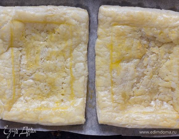 Противень выстелить бумагой для выпечки, выложить тесто, сделать легкий надрез в виде квадрата, смазать поверхность желтком и выпекать в духовке 8–10 минут, до золотистого цвета.