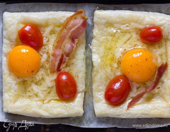 Достаньте пирог из духовки, и немного надавите на внутреннюю часть. Аккуратно выложить в центр тертый сыр, бекон и помидоры черри. Разбейте яйца в середину каждого пирога, верните в духовку еще на 10-15 минут, или до готовности яиц.