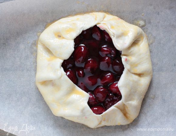 Противень выстелить бумагой для выпечки, смазать сливочным маслом, и выложить тесто. Аккуратно выложить вишню в центр теста, отступив примерно 1-2 см от края, затем подверните края внутрь, слегка прикрыв начинку, защипните края. Смазать взбитым яйцом с молоком. Выпекайте 20 25 минут, пока тесто не станет золотистым.