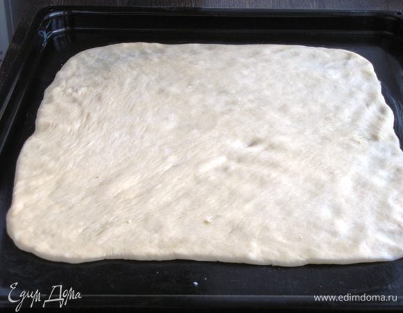 Тесто обмять, отделить небольшой кусочек для декора, остальное разделить на две равные части. Одну часть раскатать на присыпанном мукой столе, придавая форму квадрата. Перенести тесто при помощи скалки на противень, смазанный сливочным маслом.