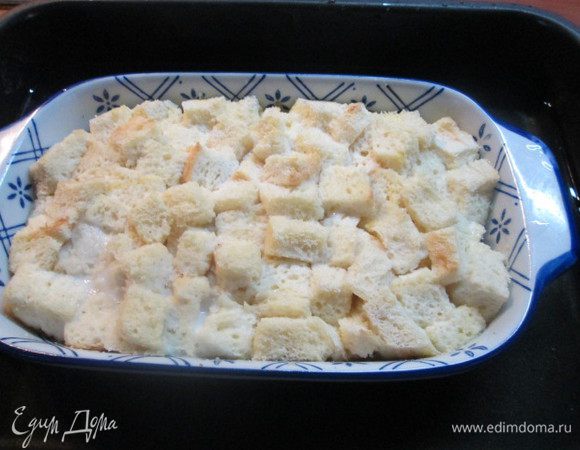 Кладем в отдельную миску кубики хлеба.
Заливаем их смесью молока, слегка взбитых яиц и ванили. Перемешиваем все тщательно и выкладываем в форму для запекания поверх изюма с сахаром.
Форму ставим в другую форму, большего размера, наполненную горячей водой. И отправляем в духовку на решетку.