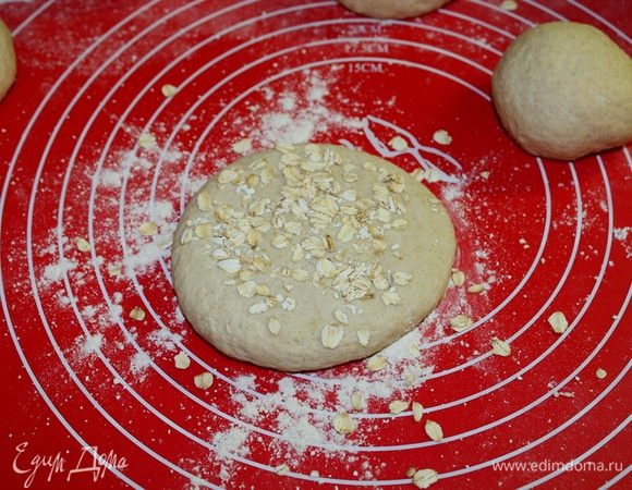 Затем расплющите каждую булочку в лепешку, смочите водой и посыпьте хлопьями.