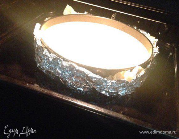 Теперь берем форму с тестом и оборачиваем её фольгой из двух слоев с низу и по бокам, так как мы будем выпекать чизкейк как бы на пару, чтобы при выпекании вода не попала и наше тесто не намокло.
Я обычно беру большую фольгу, чтобы не скреплять ее между собой, но если такой нет, то можно два листа фольги скрепить между собой и получится большой лист.

Аккуратно переливаем крем в форму с коржом ставим на противень и располагаем противень по середине духовки и наливаем на противень воду почти до краев. Выпекаем при 160°C 1 час 20 минут, но нужно за ним присматривать все зависит от вашей духовки, но на час минимум.

После выпекания приоткрываем духовку и даем остыть чизкейку до комнатной температуры.

Затем когда он остыл, аккуратно достаем из духовки чизкейк и вместе с формой накрываем пленкой, ставим в холодильник на ночь или на 8 часов.
