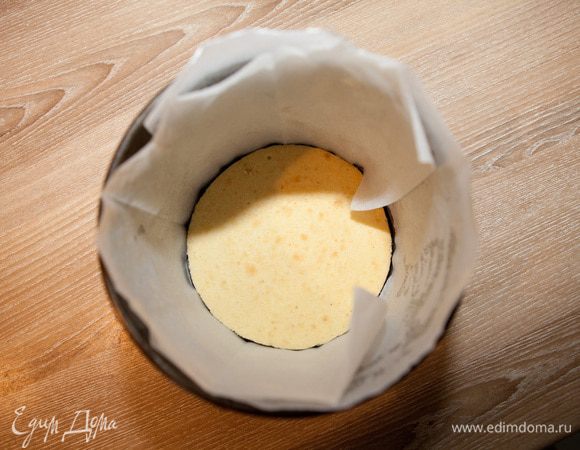 Остывший корж положите в форму. Стенки формы лучше смазать сливочным маслом и обложить слоем пекарской бумаги.