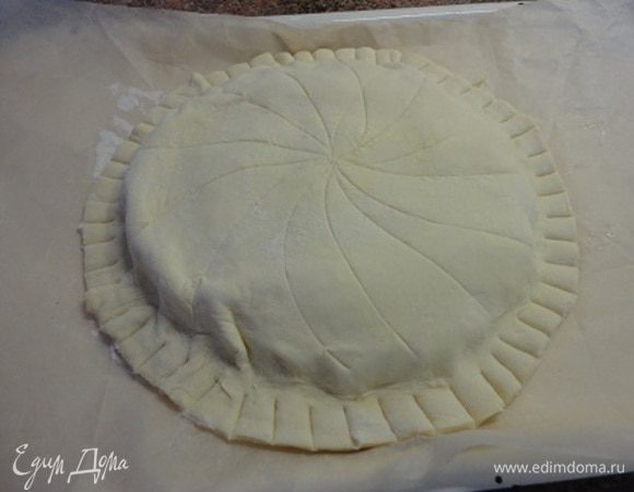 Оставшееся тесто раскатать и вырезать круг чуть больше первого. Вынуть основу из холодильника. Оставшееся яйцо слегка взбить вилкой и смазать свободные края нижнего пласта теста. Затем накрыть вторым кругом. Плотно скрепить края, сделать насечки на ребре пирога и в виде веера — на поверхности. Поставить в холодильник на 1 час.