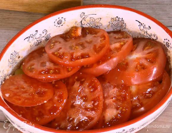 Жаропрочную керамическую форму смазать оставшимся сливочным маслом, посыпать дно и бока частью молотых сухарей, выложить обжаренный лук и чеснок, сверху поместить кружки помидоров.