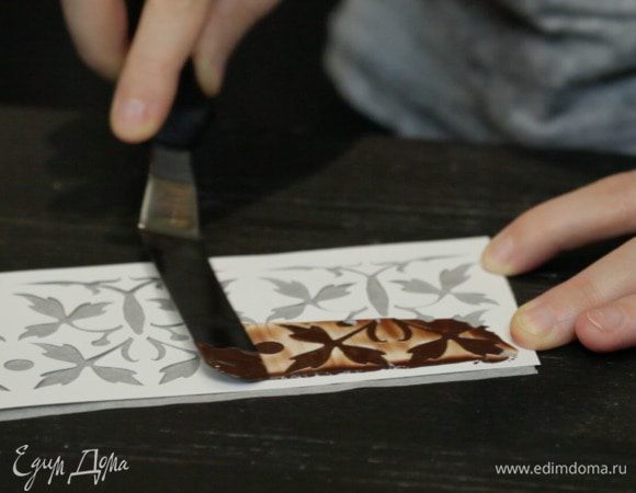 На этом торт готов. Но я решила ещё сделать ажурный бортик из шоколада. Для этого понадобится трафарет, пекарская бумага и немного шоколада или глазури.

Растапливаем шоколад/глазурь, вырезаем по форме полоску пекарской бумаги. Сверху кладём трафарет и с помощью шпателя распределяем и убираем излишки шоколада по трафарету.

Оставляем шоколад немного застыть.