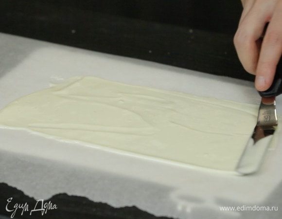 Из белого шоколада или глазури делаем декор. Для этого растапливаем шоколад и распределяем шпателем по пекарской бумаге. Убираем в холодильник до застывания.