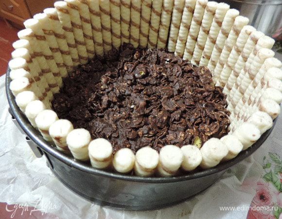 К этому времени у нас уже готова разъемная форма диаметром 20 см, дно которой выстелено пергаментом. Выкладываем туда шоколадную смесь, разравниваем, утрамбовываем, устанавливаем плотно друг к дружке вафельные трубочки (если их используете) и отправляем в холодильник.